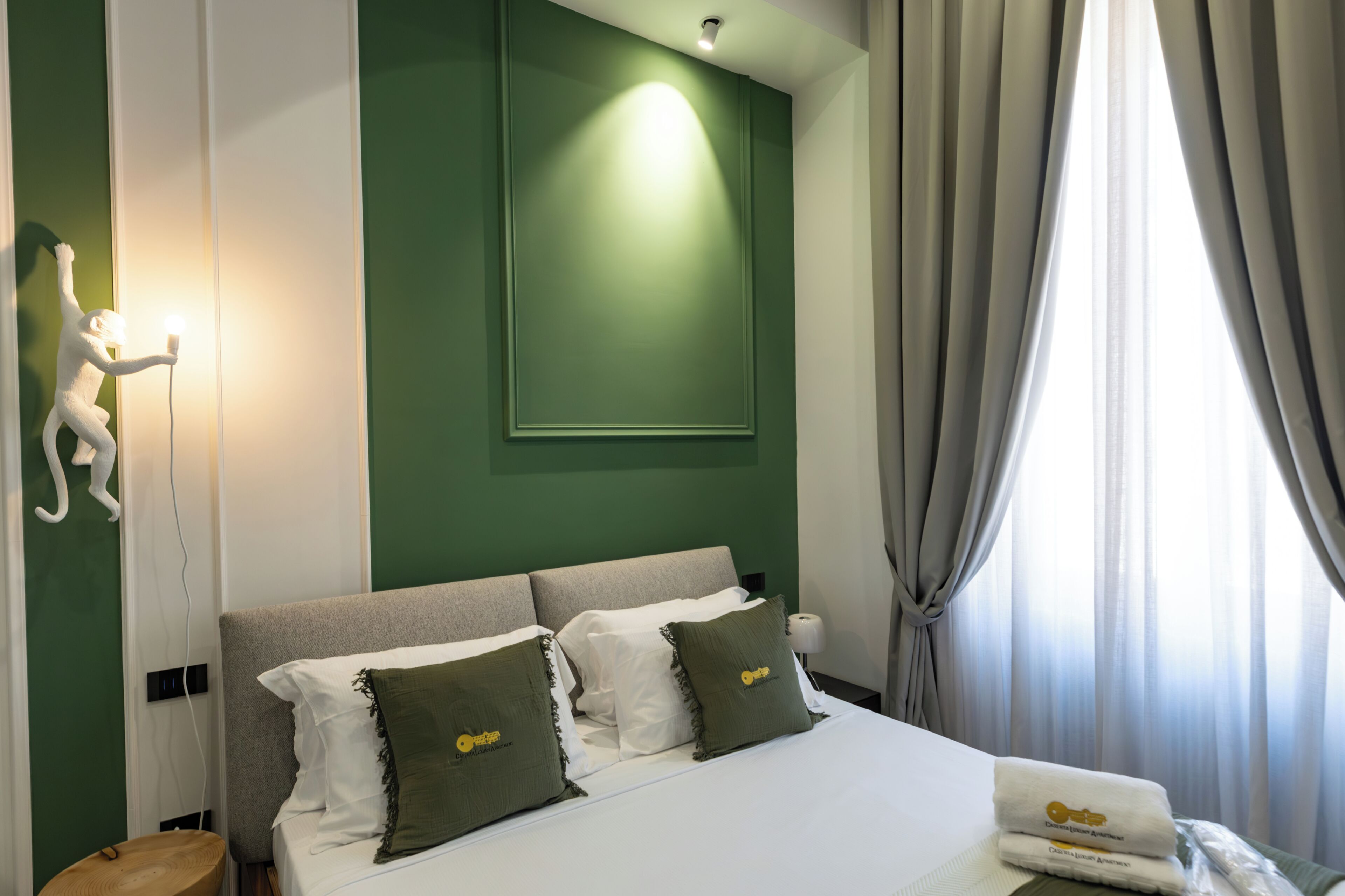 Ein Hotelzimmer mit einem Bett, Kissen, einem Nachttisch, einer Wandleuchte und einem Vorhangfenster.