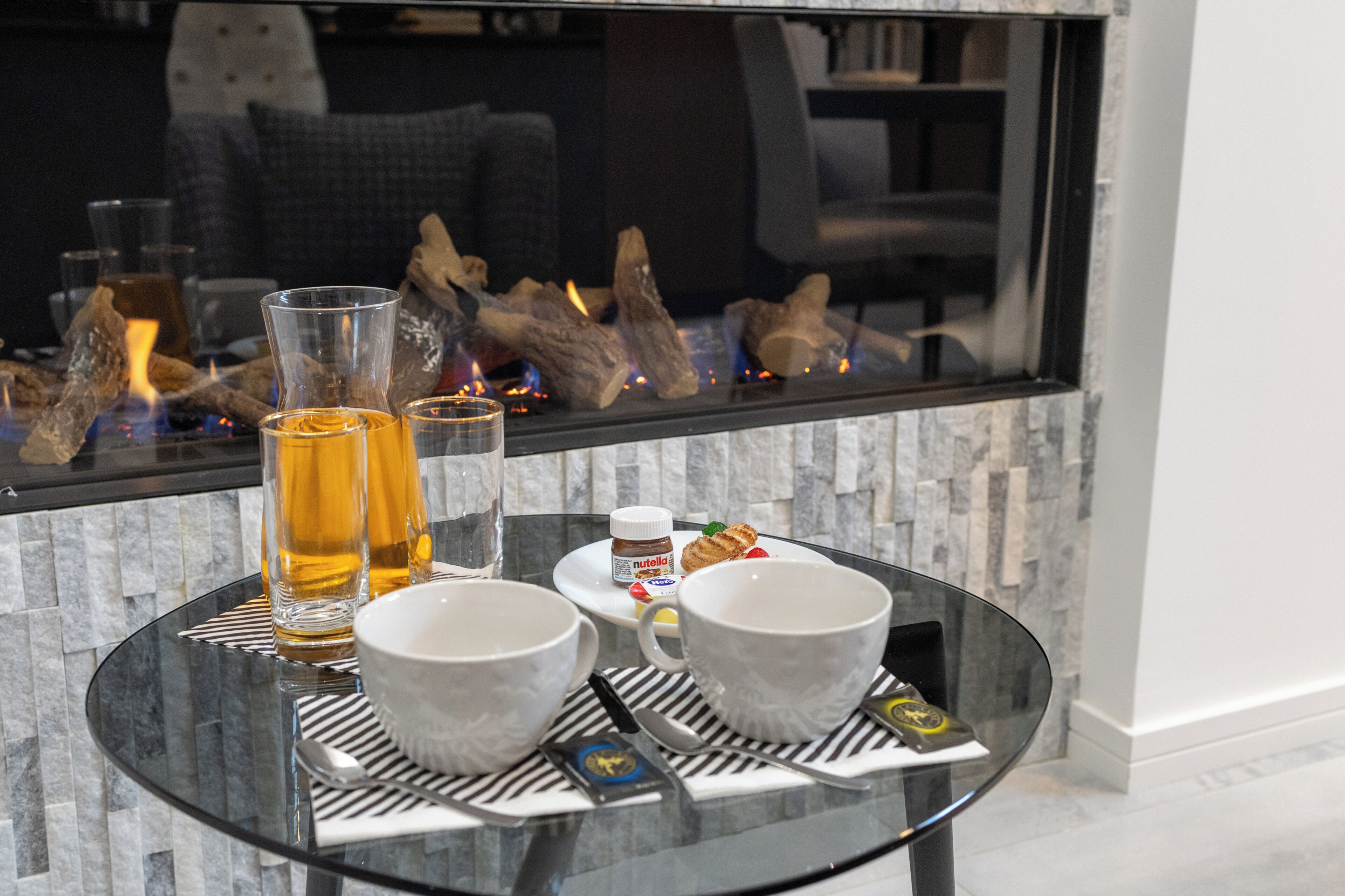 A glass table with a bottle, two cups, and a jar of Nutella.