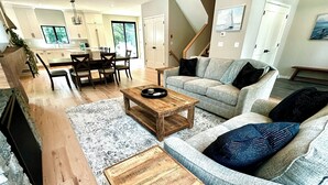 Ein geräumiger Wohnbereich mit einem Holztisch, einem grauen Sofa mit gemusterten Kissen und einem Essbereich mit Holztisch und Stühlen.