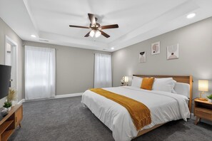 A bedroom with a bed, a ceiling fan, a TV, and a nightstand with a lamp.