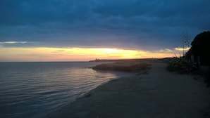 Een strand bij zonsondergang, met rustige zee en een rotsformatie.