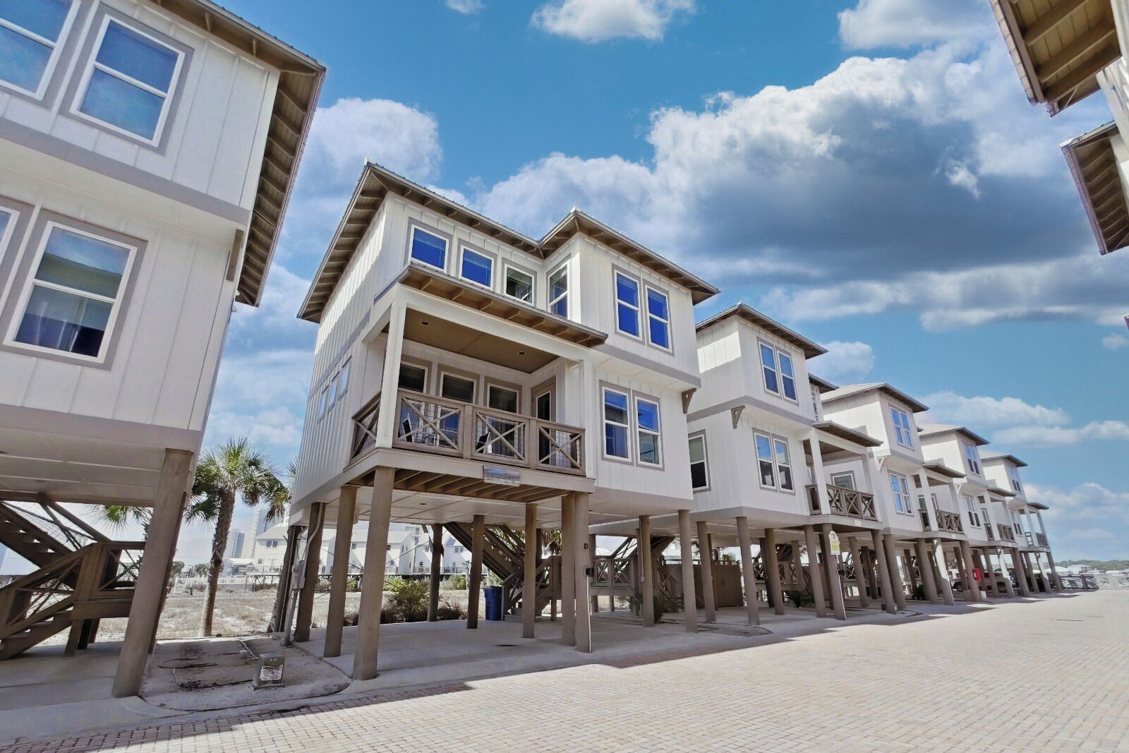 A beachfront property with elevated structures, a paved walkway, and palm trees.