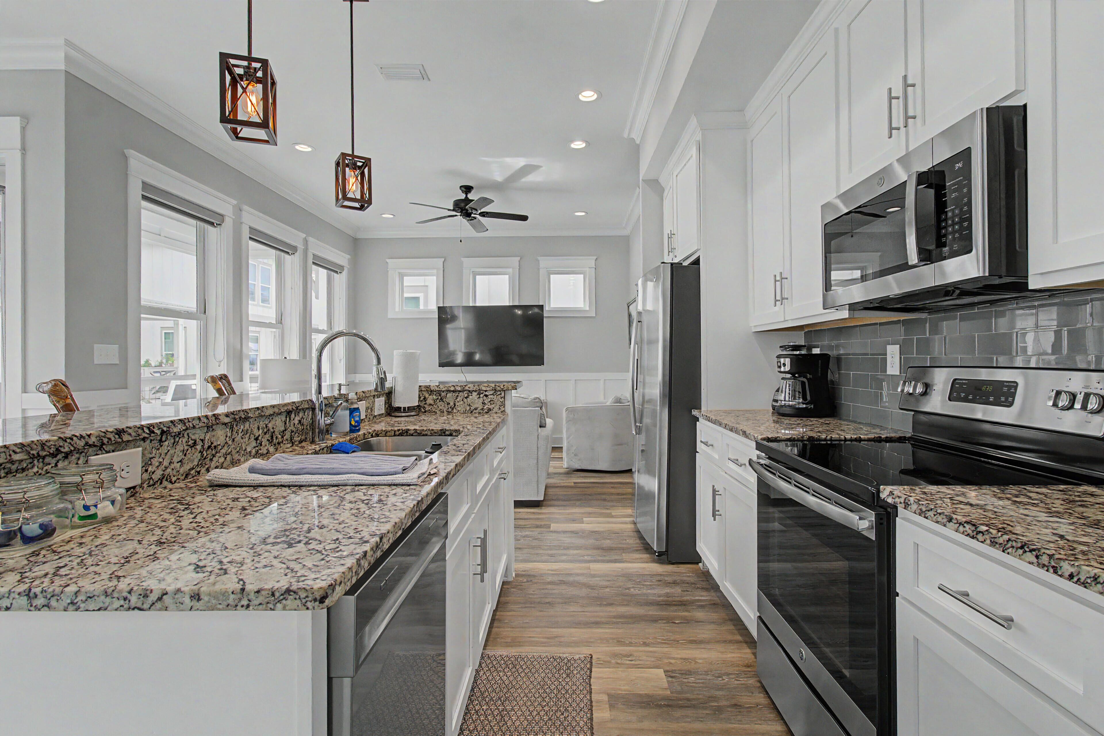 A modern kitchen with white cabinets, granite countertops, a stainless steel refrigerator, a microwave, and an oven.