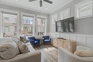 A spacious living room with a large flat-screen TV, two blue armchairs, a beige sofa, and a wooden cabinet. - Cottages at Lagoon Pass D | Walk to the Beach (Gulf Shores)