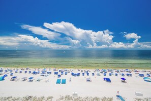 Een strand met tal van parasols en ligbedden, een helderblauwe lucht en de oceaan.
