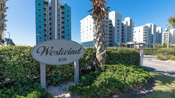 Skilt for Westwind 939, omgivet af grønt og palmer, med moderne højhuse i baggrunden.
