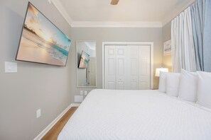 Een hotelkamer met een groot bed, een schilderij van een strandtafereel, een deur en een spiegel.