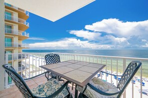 Een balkon met een tafel en stoelen, uitkijkend op een strand met parasols en mensen.
