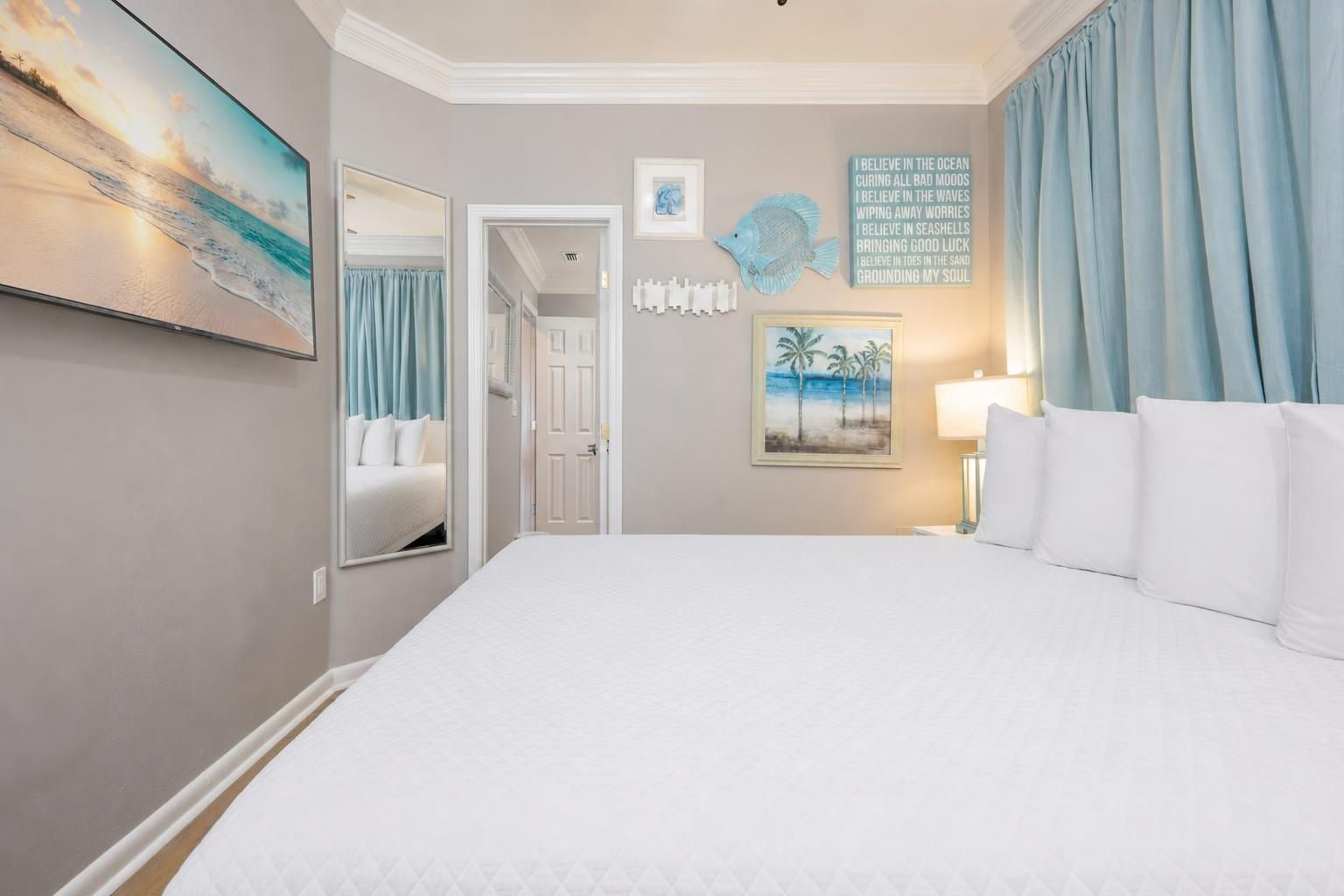 Ein Hotelzimmer mit einem großen Bett, einem Strandbild, einer Wand mit einem Zitat über das Meer und einer Tür zu einem anderen Raum.