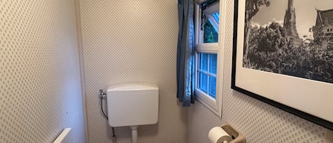 A small bathroom with a toilet, a window with curtains, and a framed picture on the wall.