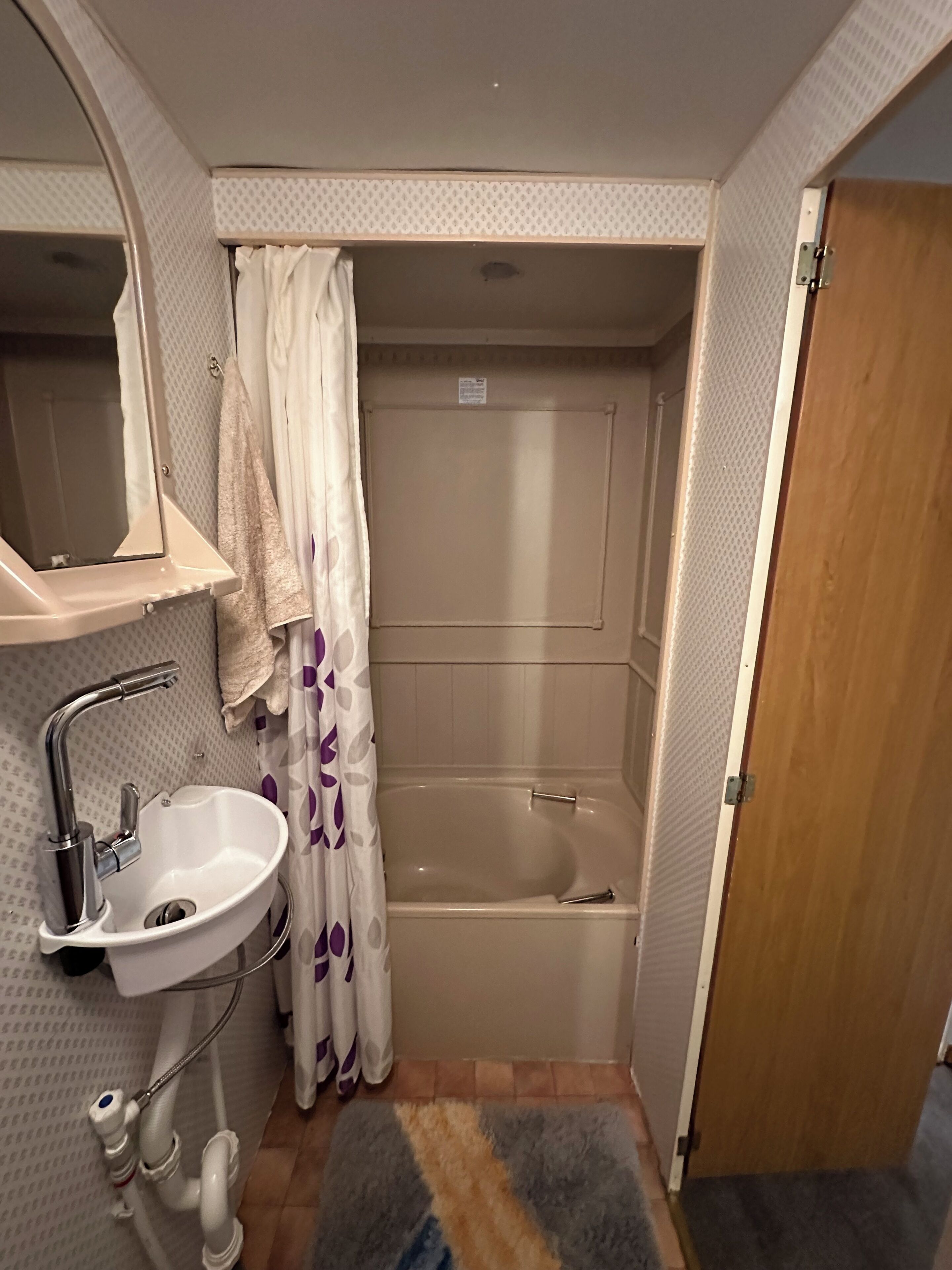 A bathroom with a sink, mirror, shower curtain, and bathtub.