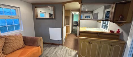 A compact living space with a sofa, a small table, a mirror, and a kitchenette area.