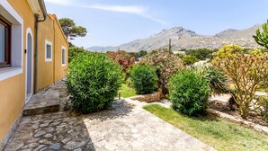 A stone pathway leading to a building with a yellow facade, surrounded by greenery and mountains in the background. - Villa "Alexandria" with Mountain View, Pool, A/C, Terrace & Garden (Cala Sant Vicenç)