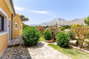 A stone pathway leading to a building with a yellow facade, surrounded by greenery and mountains in the background. - Villa "Alexandria" with Mountain View, Pool, A/C, Terrace & Garden (Cala Sant Vicenç)