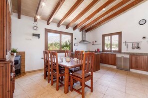 Een ruime keuken met houten kastjes, een centraal eiland en een eetgedeelte met houten stoelen.