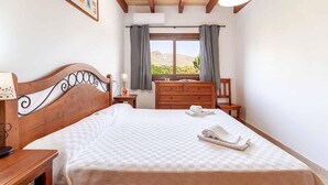A bedroom with a wooden bed, a dresser, a chair, a nightstand, and a window with a view of the outdoors. - Villa "Alexandria" with Mountain View, Pool, A/C, Terrace & Garden (Cala Sant Vicenç)