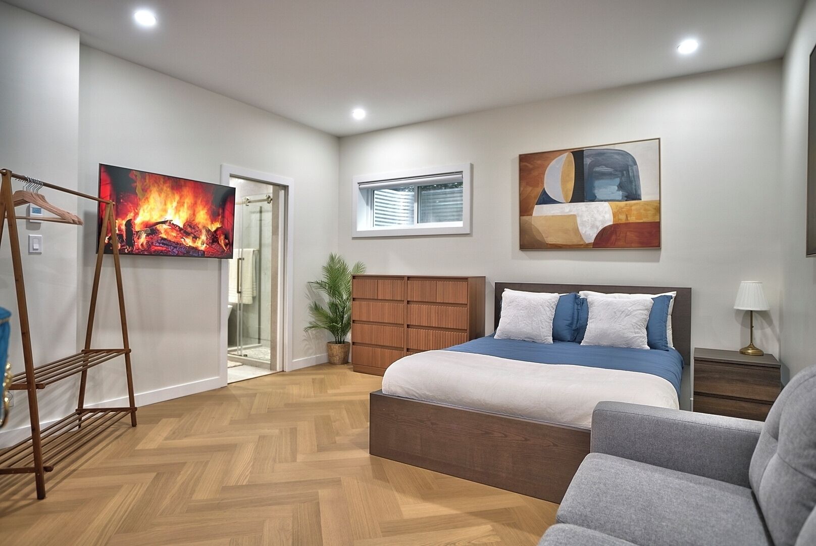 A bedroom with a bed, a TV, a plant, and a painting.