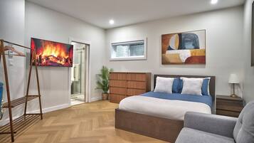 A bedroom with a bed, a TV, a plant, and a painting.