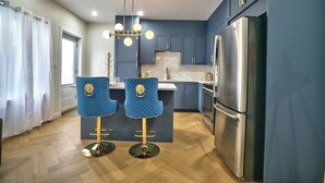 Eine moderne Küche mit einer zentralen Kochinsel, zwei Barhocker, einem Edelstahlkühlschrank und blauen Schränken.