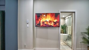 Ein Zimmer mit flachbildfernseher an der Wand, Holzboden und Glastür zu einem Badezimmer mit Badewanne.