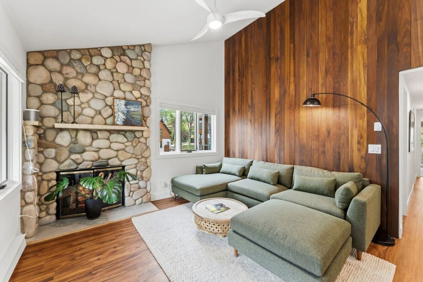 Un salón con pared de piedra, paneles de madera, un sofá modular, una mesa de centro redonda y una chimenea.