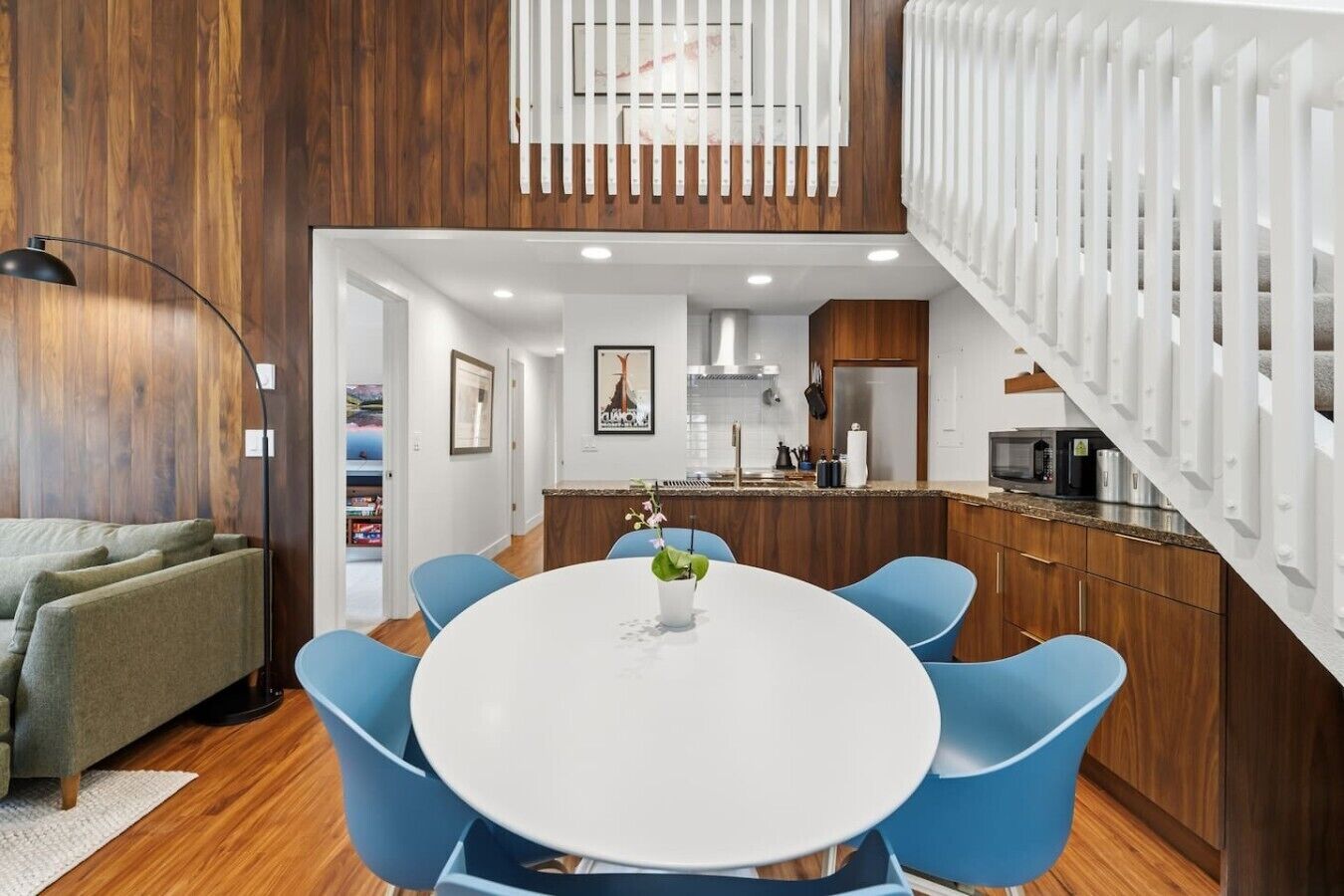 Ein modernes Interieur mit einem runden Esstisch, blauen Stühlen, einer Couch und einer Küchenzeile, sowie einer Treppe.