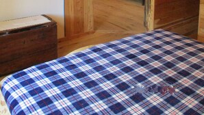 Habitació rústica amb sostre de fusta, un llit amb colcha escocesa, paret de pedra i una porta que dona a una altra habitació.
