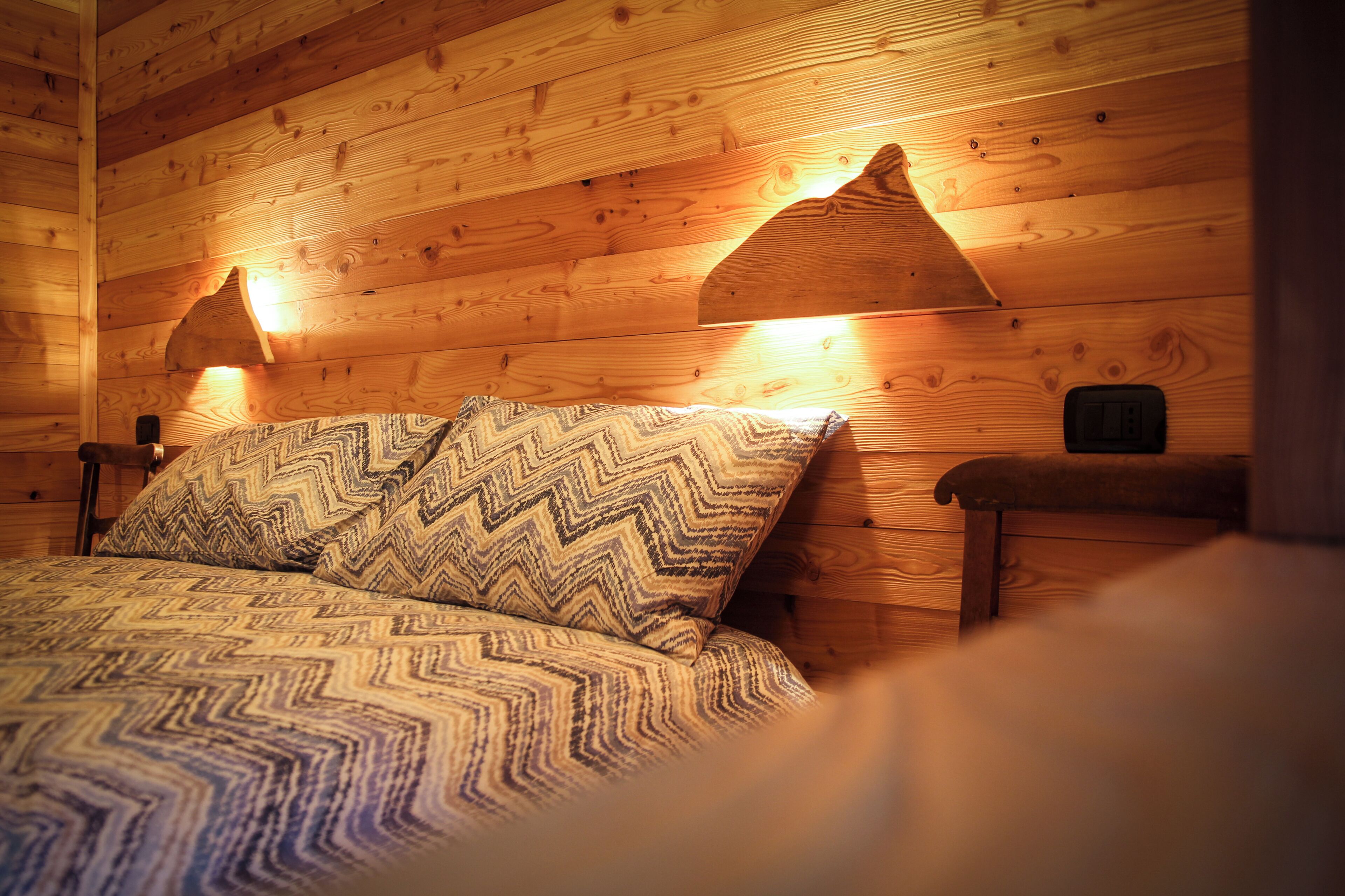 A wooden cabin room with a bed, two wall-mounted lamps, and a bench.