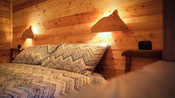 A wooden cabin room with a bed, two wall-mounted lamps, and a bench.