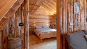 A wooden cabin interior with a bed, a wooden barrel, and a wall-mounted light fixture.