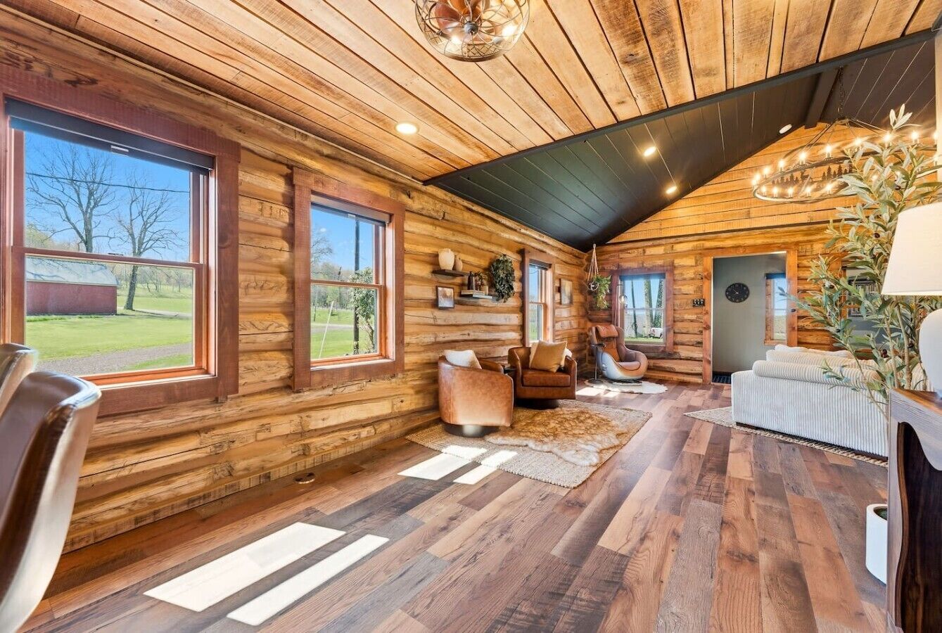 Een blokhutinterieur met houten wanden, grote ramen, een open haard en een kroonluchter.