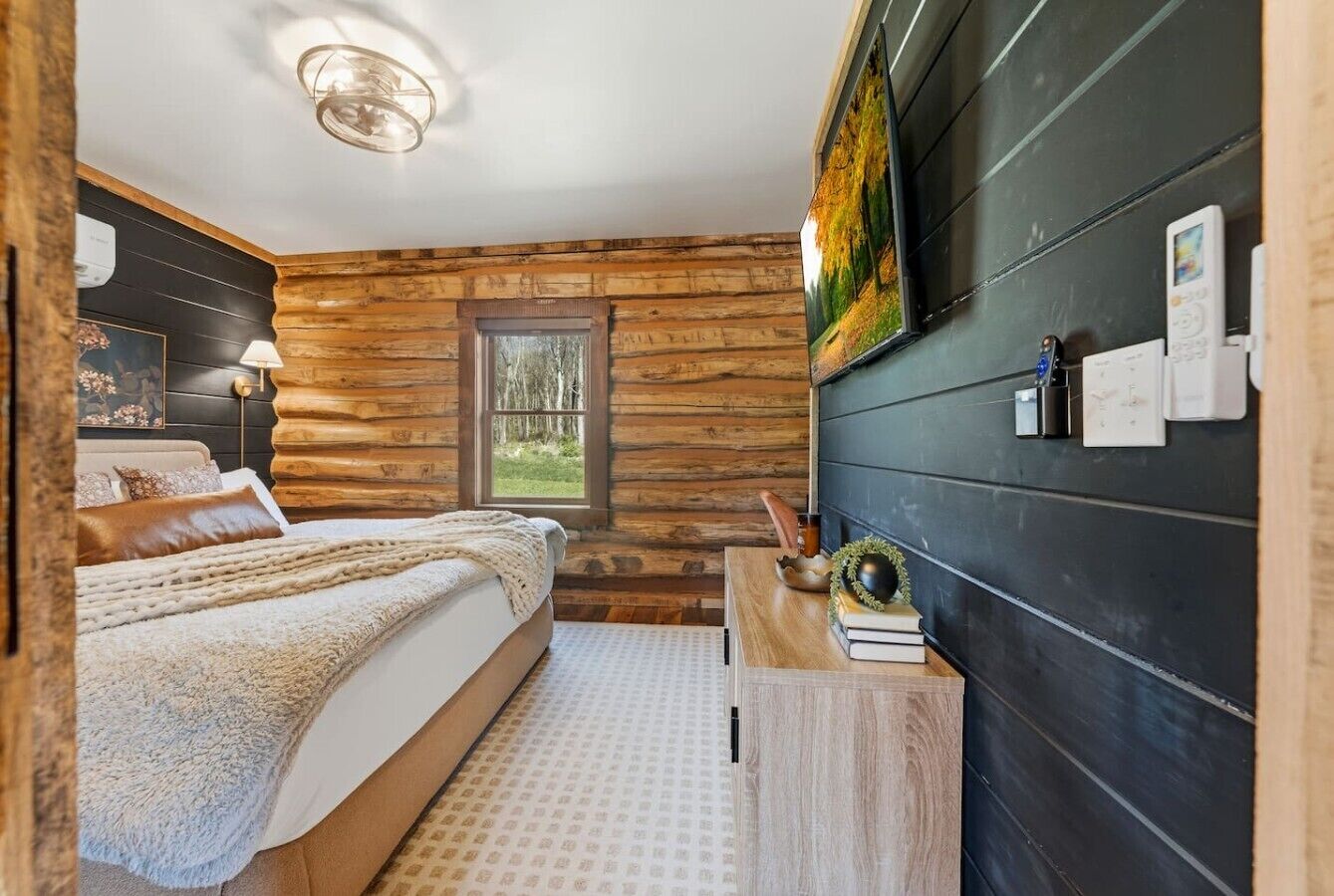 Een slaapkamer in een blokhut met een bed, een nachtkastje, een tv aan de muur en een raam.