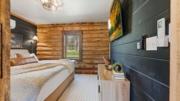 Een slaapkamer in een blokhut met een bed, een nachtkastje, een tv aan de muur en een raam.