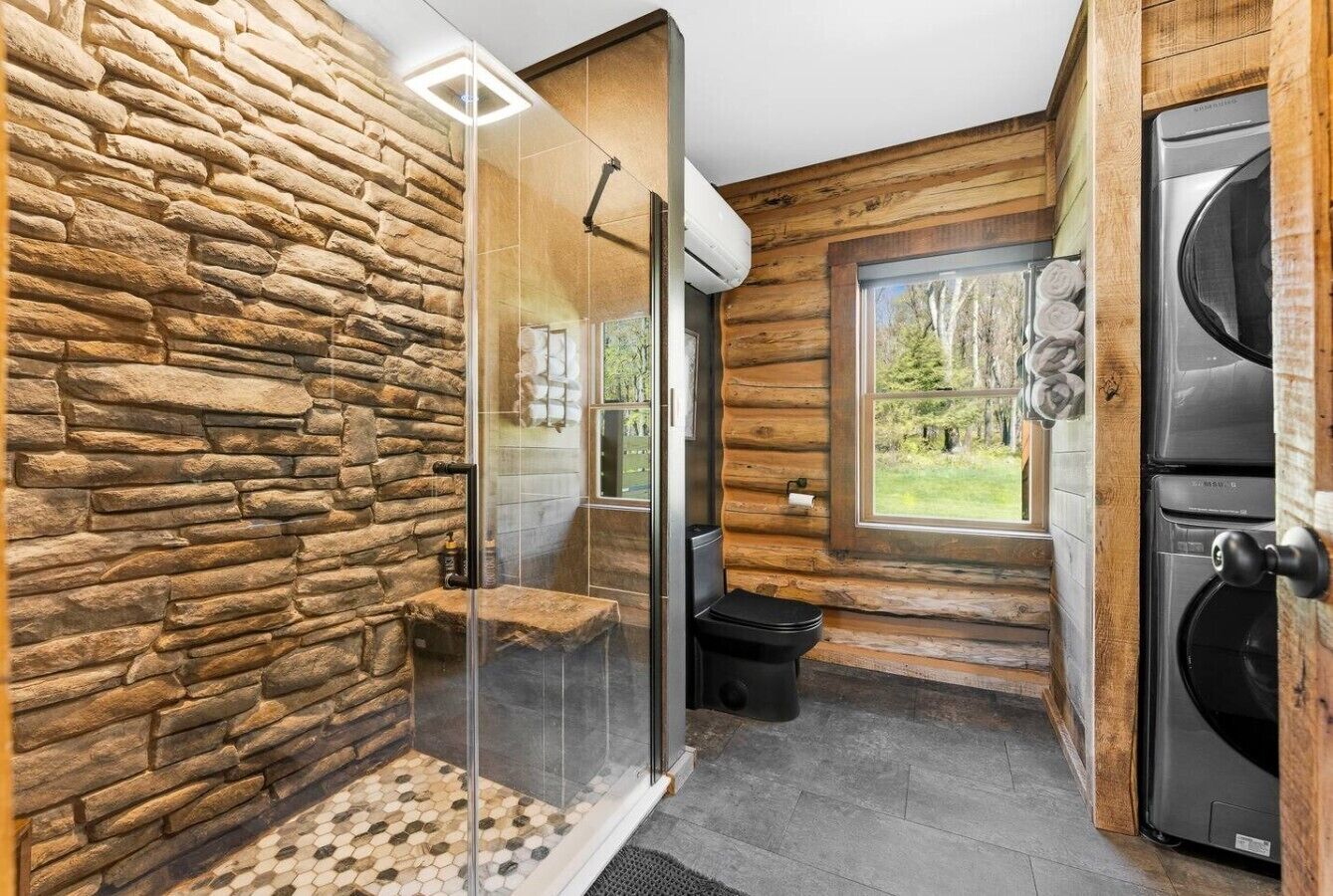 A bathroom with a stone wall, a glass shower enclosure, a toilet, and a washing machine.