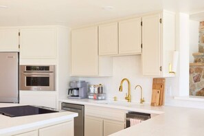 Een moderne keuken met witte kastjes, roestvrijstalen apparatuur, een koffiezetapparaat en een accentmuur van steen.