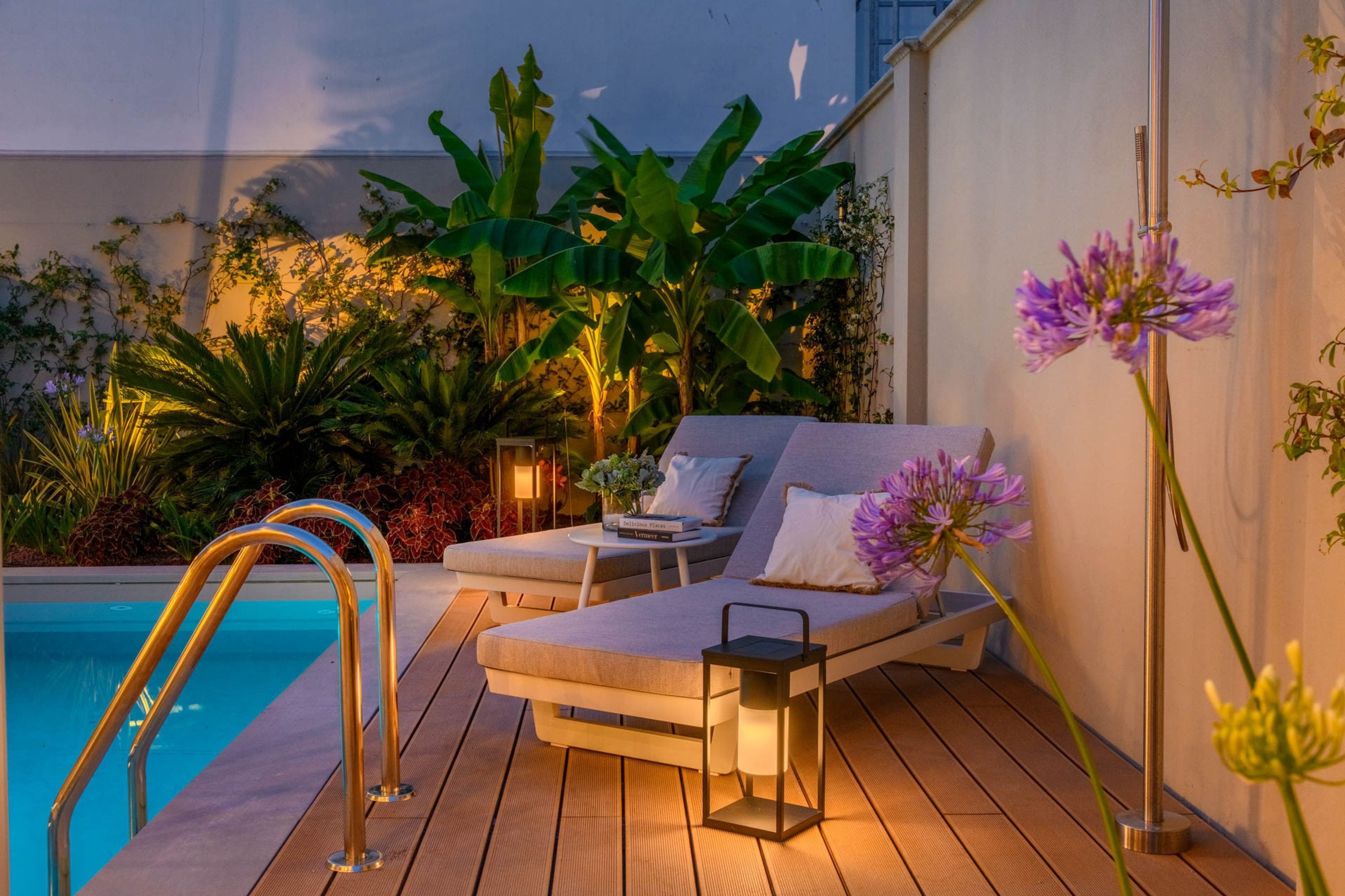 A poolside area with a lounge chair, a small table with a book, and a lantern.