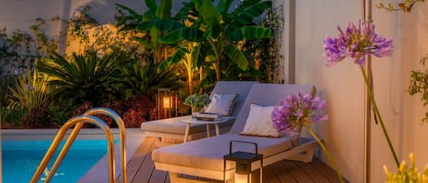 A poolside area with a lounge chair, a small table with a book, and a lantern.
