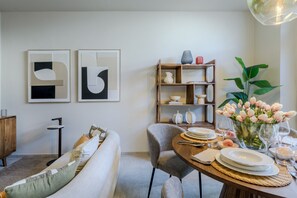 Ein Essbereich mit einem runden Tisch für vier Personen, einer Couch, einem Bücherregal und zwei abstrakten Bildern an der Wand.