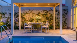 Uma área de refeições coberta ao ar livre com uma piscina em primeiro plano.