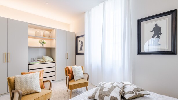 Quarto moderno com uma cama, duas cadeiras, um guarda-roupa e uma janela grande com cortinas.