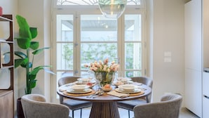 A dining area with a round table set for four, surrounded by chairs, a vase of flowers, and a hanging light fixture.