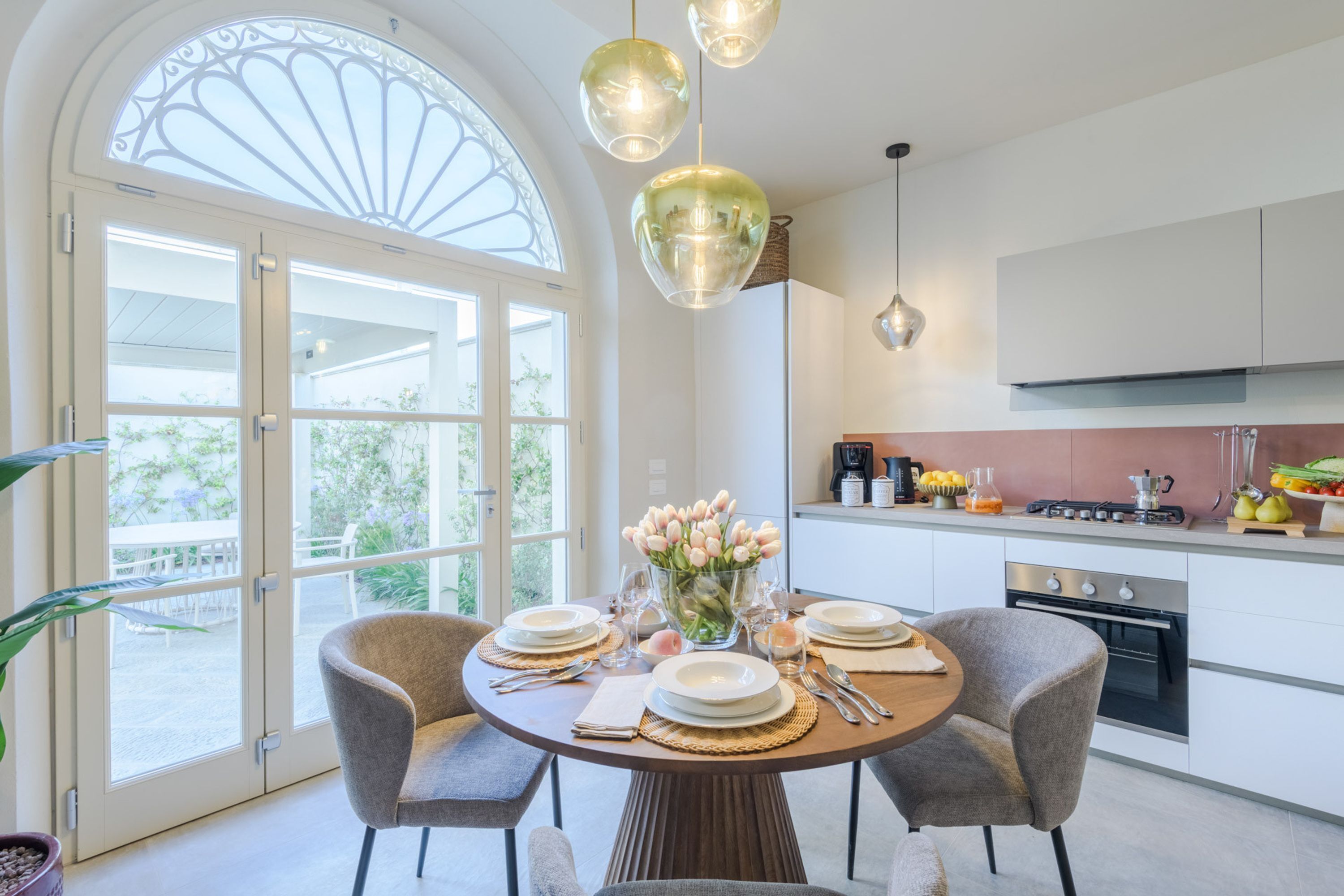 A modern kitchen with a dining area, large windows, and a view of greenery.
