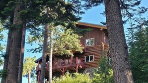 Une cabane en rondins dotée d’un balcon, entourée de grands arbres.