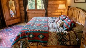 Une chambre dans une cabane en bois, avec un lit, une fenêtre, une lampe et un tableau encadré au mur.