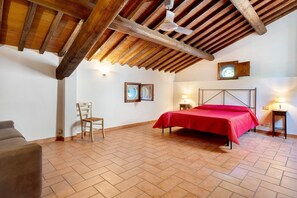 A bedroom with a wooden ceiling, a bed with a red bedspread, a chair, two bedside tables with lamps, and a wall-mounted clock. - Apartment 16 - La Ferriera residence with pool (Loro Ciuffenna)