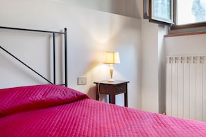 Ein Hotelzimmer mit Bett, Nachttisch, Lampe, Fenster und Heizkörper.