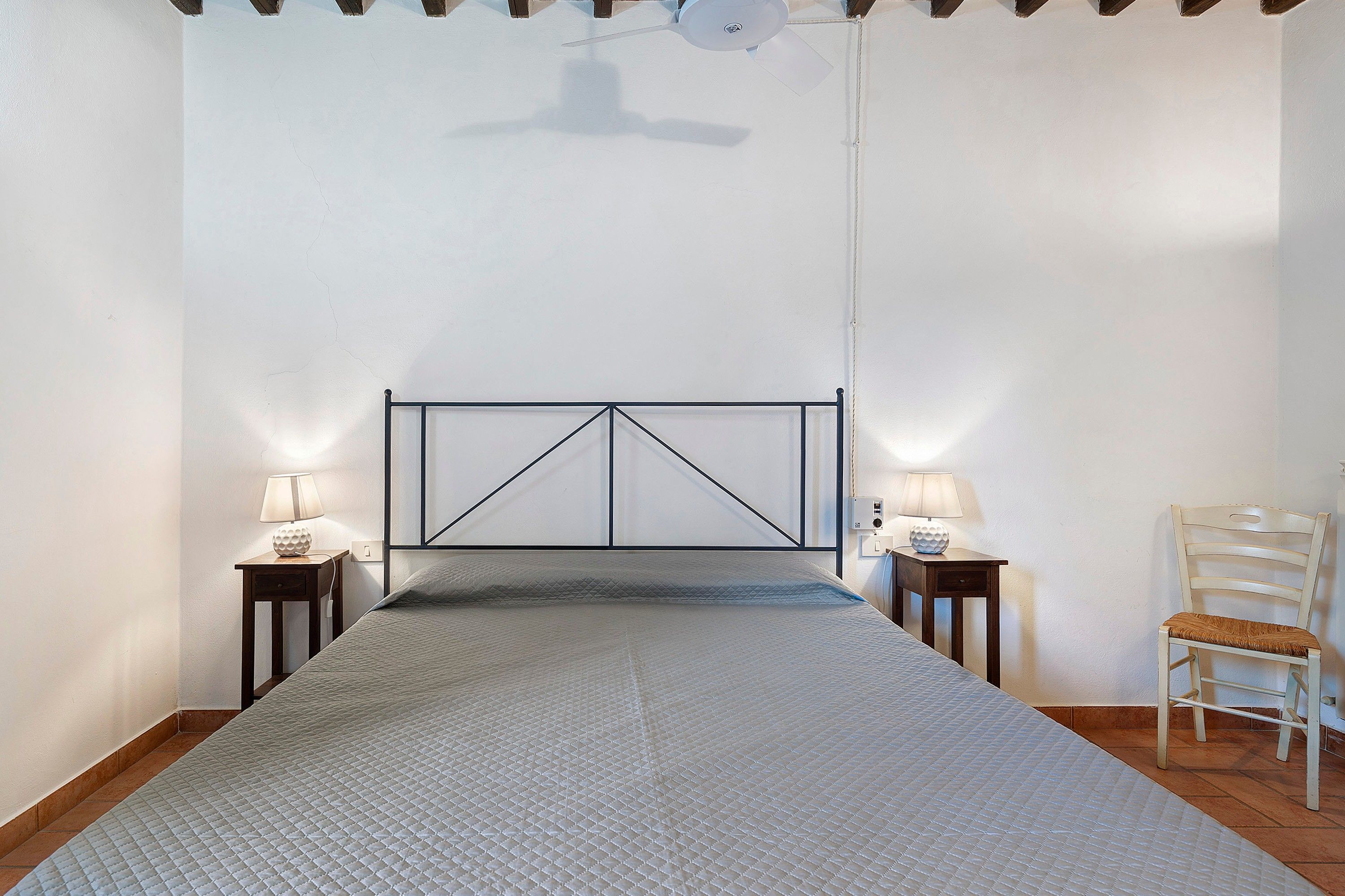 A bedroom with a bed, two bedside tables with lamps, a chair, and a ceiling fan.