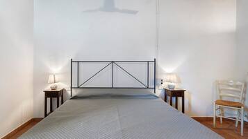 A bedroom with a bed, two bedside tables with lamps, a chair, and a ceiling fan.