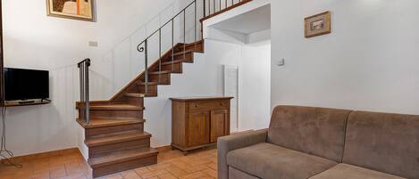 Una escalera con escalones de madera y barandillas de metal, un televisor de pantalla plana sobre un mueble, un sofá de cuero marrón y un armario de madera.