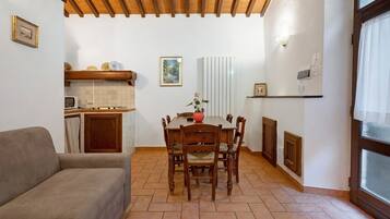 Ein gemütlicher Wohnbereich mit Esstisch, Stühlen, einer Couch, einer Küchenzeile und einem Fenster mit Vorhängen.